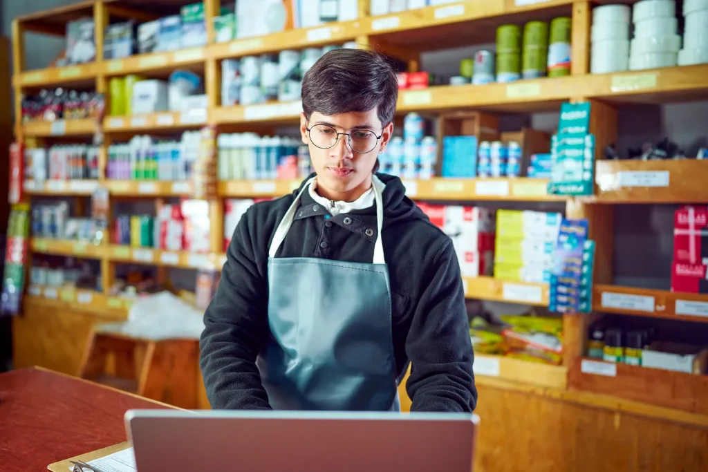 Google Business Profile Optimisation 2026 (Shop owner using a laptop behind the shop counter)